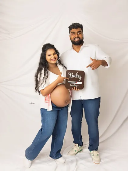 A cute announcement shot with a "Baby Loading" sign. The couple's casual white shirts and jeans create a relaxed and modern vibe.