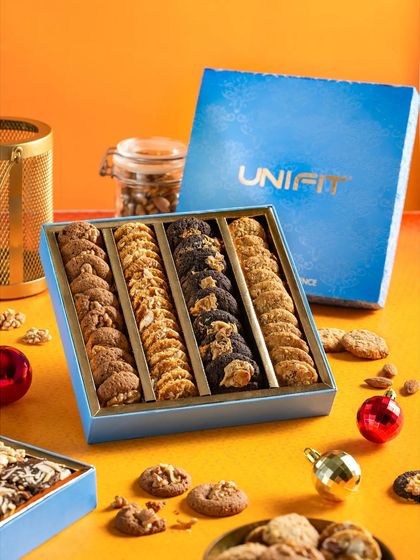 A large gift box of assorted Unifit cookies, styled with Christmas ornaments for a festive gifting theme.