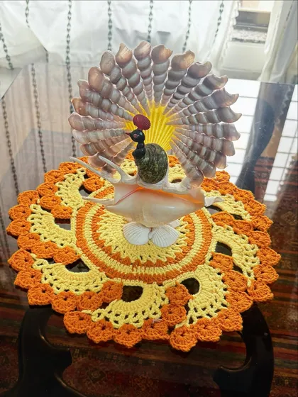 This vibrant orange and yellow crochet doily, shown here as a base for a decorative piece, adds a burst of color and handmade charm to any tabletop.