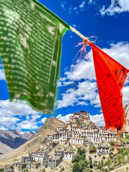 A view of the iconic Key Monastery in Spiti Valley, framed by colorful Buddhist prayer flags. The flags carry prayers on the wind, adding to the spiritual atmosphere of the place.