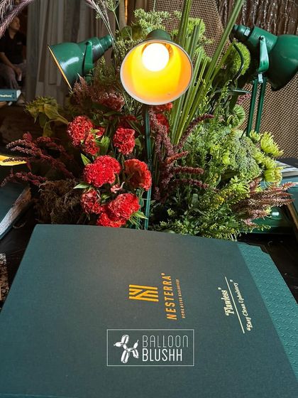 A creative centerpiece combining red carnations and greenery with unique green desk lamps, designed to highlight Nesterra's product lookbooks.