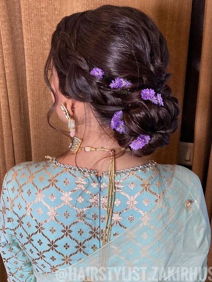 A close-up of the braided low bun with purple flowers, showing the delicate floral accents.