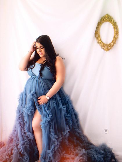 A confident solo pose in a dramatic blue gown. The high slit and flowing fabric create a stunning, high-fashion look for this maternity portrait.
