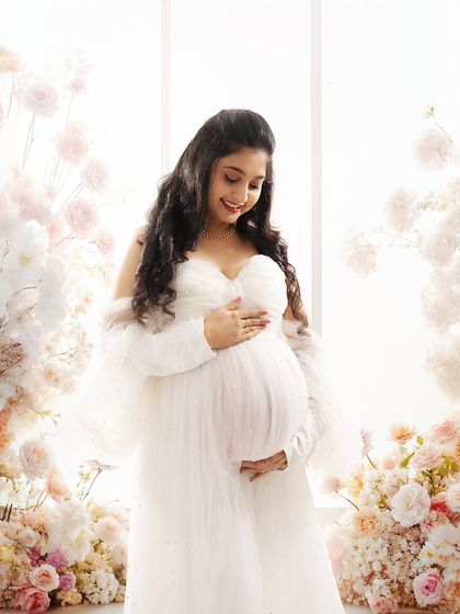 A close-up shot capturing the joyful smile and pregnancy glow of the mother-to-be, surrounded by a beautiful floral arch.