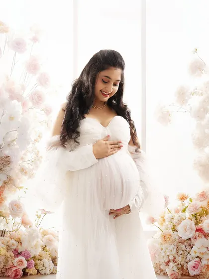 A close-up shot capturing the joyful smile and pregnancy glow of the mother-to-be, surrounded by a beautiful floral arch.