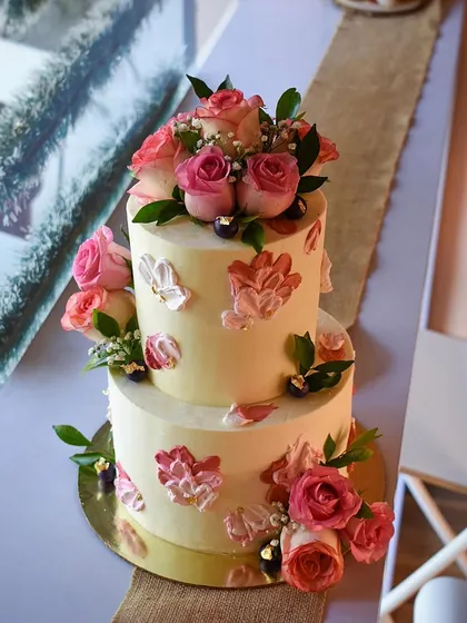 A white chocolate engagement cake with a lovely peach and pink floral theme. The design features hand-painted floral motifs and is decorated with beautiful fresh roses, creating a soft and romantic look.