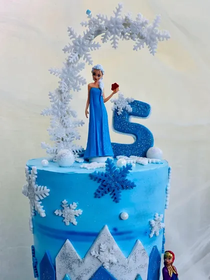 A two-tier Frozen cake featuring an Elsa doll and a sparkling number 5 topper.