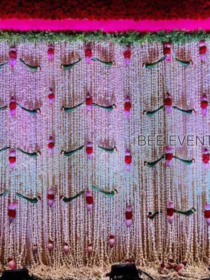 A stunning backdrop for a naming ceremony, made entirely of fresh flowers. The wall of white tuberoses is accented with hanging floral parrots and lotus buds, creating a fragrant and beautiful setting.