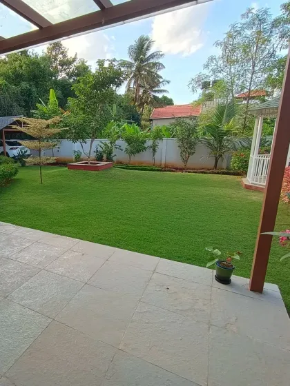 A wide view of a total landscape makeover, featuring a large, manicured lawn viewed from a stone patio. The design includes a white gazebo and colorful flower beds along the property line.