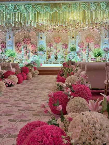 The view down the aisle, lined with large floral spheres in shades of pink and cream. The custom-printed carpet adds another layer of bespoke detail to the decor.