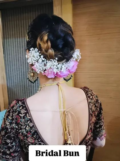 This is a classic bridal bun, intricately woven and adorned with a combination of fresh pink roses and delicate baby's breath. It's a secure and elegant choice that keeps the focus on the bride's profile and jewelry.