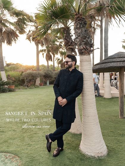 Sangeet in Spain, where two cultures dance as one. The groom looks effortlessly cool in a midnight blue Manish Malhotra achkan, a classic choice that balances his bride's vibrant outfit.
