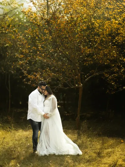An intimate moment of love and anticipation. The couple is framed by the beautiful autumn colors of the trees, with the soft, golden light creating a warm and romantic atmosphere.