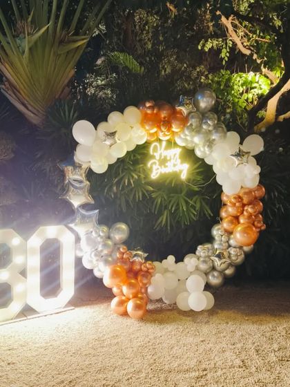 An elegant outdoor setup for a 30th birthday. I used a ring of white, silver, and rose gold balloons, a neon sign, and large marquee numbers, all beautifully lit for a nighttime celebration.