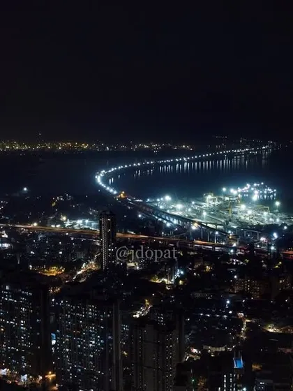 An aerial night view of Mumbai, showing the illuminated Trans Harbour Link stretching across the water.