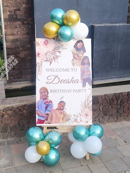 A personalized welcome board on an easel for a birthday party, decorated with balloons.