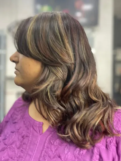A side view of a layered haircut with bangs and soft waves. The highlights add depth and dimension to this chic, shoulder-length style.