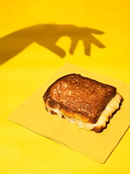 A single grilled cheese sandwich on a yellow napkin, with the shadow of a hand reaching for it. This creative and playful shot uses shadows to tell a story and create intrigue.