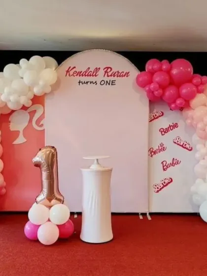 A stylish Barbie-themed setup for a first birthday, featuring a clean design with a Barbie silhouette and logo on the backdrop.