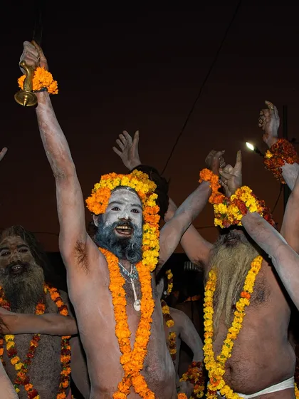 Naga sadhus celebrating at the Kumbh Mela, their faces painted and bodies adorned with garlands. Their expressions are of pure joy and spiritual fervor.