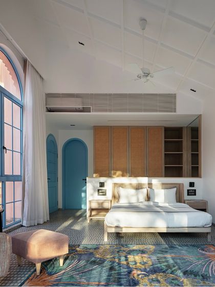 This bedroom at Baia Villas is a blend of Goan vibrancy and serene comfort. The large arched window with its blue frame is a signature element, while the wooden furniture and patterned rug add warmth and texture.