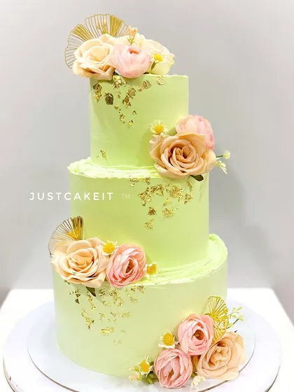 An elegant three-tier reception cake in a lovely pastel green. The design is accented with gold leaf and beautiful peach and pink sugar flowers.