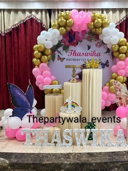 A lovely butterfly theme with a pink, white, and gold balloon arch against a red curtain backdrop. The large butterfly cutouts add a beautiful touch.