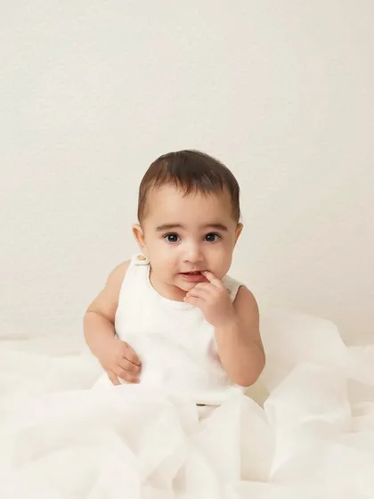 A curious baby boy in a simple white outfit, looking thoughtful. The clean, minimalist setup puts all the focus on his sweet expression.