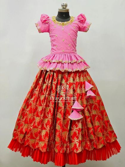 A festive red and pink Banarasi lehenga. The blouse has a tiered peplum design, and the skirt is made from a rich brocade fabric.