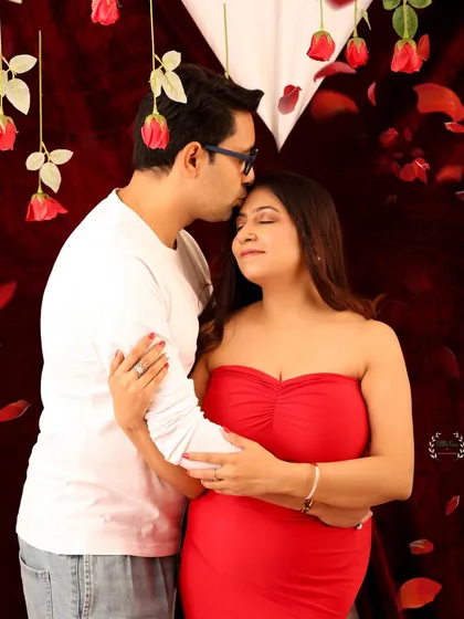 A gentle kiss on the forehead. This close-up shot from a Valentine's maternity session focuses on the tender connection between the expecting parents, surrounded by a romantic red theme.