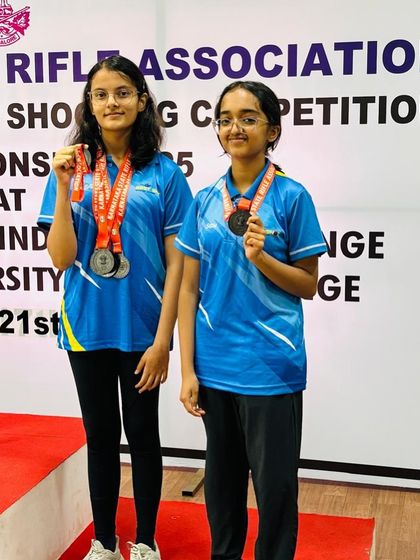 Indu and Bhuumika, two of our decorated air rifle athletes, standing together with their medals after a successful state-level competition.