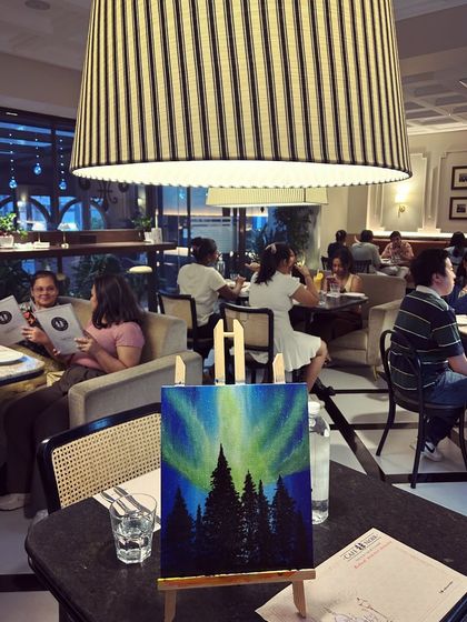 A finished northern lights painting sitting on an easel in a bustling cafe, showing how art can be created anywhere.