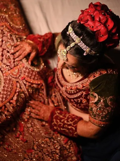 An artistic top-down shot of the bride admiring the intricate embroidery of her wedding lehenga.
