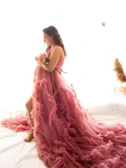 A full-length shot of a mother-to-be in a dramatic pink ruffled gown, creating a beautiful silhouette against the bright window light.