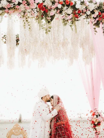 A romantic kiss on the forehead under a shower of petals. The bride's makeup looks soft and dreamy, creating a truly magical wedding portrait.