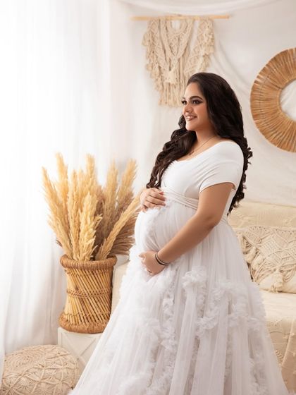 A profile shot capturing the serene beauty of the mother-to-be as she looks out the window, surrounded by the soft textures of the boho decor.