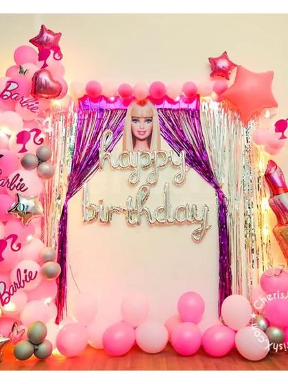 A fun and girly Barbie-themed birthday setup. The decor features a silver and purple shimmer curtain, Barbie cutouts, and lots of pink balloons.