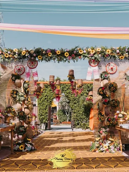 A stunning entrance for an Assamese-themed celebration. The walkway is lined with banana plants and lush floral arrangements, leading to an archway decorated with sunflowers and traditional motifs.