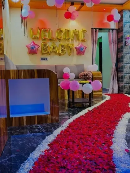 A grand "Welcome Baby" decoration featuring a long pathway of red and white rose petals. The gold foil "Welcome Baby" balloons add a celebratory touch to the entrance.