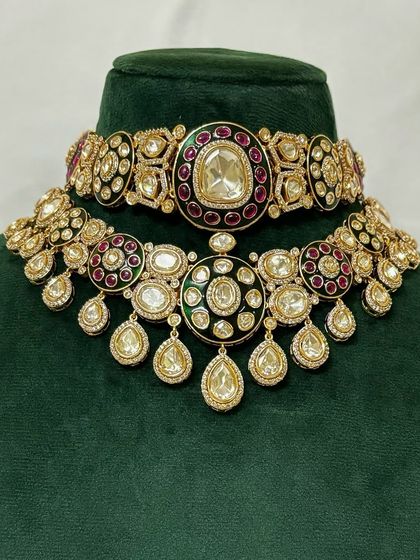 A close-up of a bridal choker and necklace set. The red and green Meenakari detailing on the Kundan work is clearly visible.