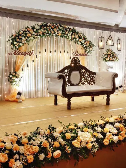 A beautiful ring ceremony stage with a floral arch of peach and white roses. The couple's names are displayed in a custom cutout, and hanging Edison bulbs add a warm, rustic-chic touch to the decor.