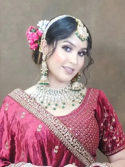 A bride in a red lehenga wearing a Kundan set with green beads. The flowers in her hair and soft makeup create a romantic look.