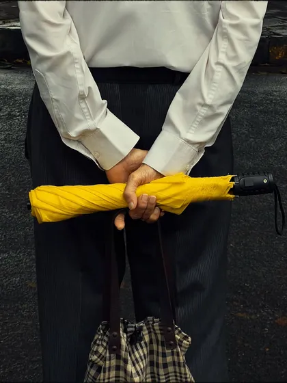 A tightly cropped, anonymous shot of a man in a formal shirt holding a closed yellow umbrella. This minimalist photo tells a story through details, color, and posture.