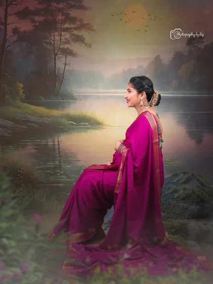 A beautiful studio portrait of a mother-to-be in a magenta saree, seated against a painted landscape backdrop.