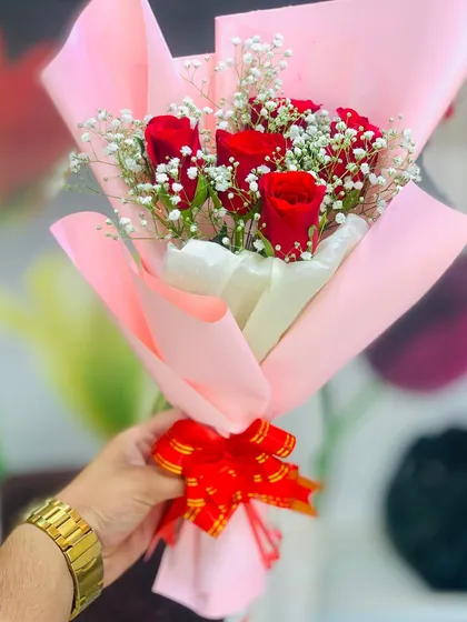 A beautifully composed photo of a classic red rose and baby's breath bouquet. The pink paper wrapping and red bow make it an ideal gift for anniversaries, Valentine's Day, or just because.