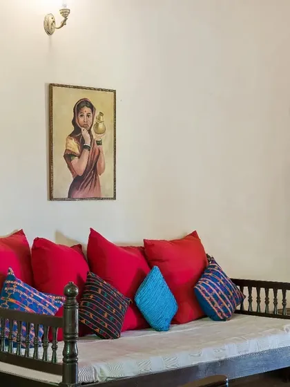 A traditional living room setup at Villa Magnolia, Coorg, with a classic wooden diwan and vibrant red cushions. The decor is rich with Indian heritage and color.