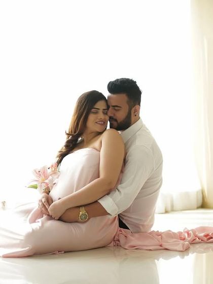 A tender embrace amidst a dreamy, high-key setup with soft pink fabrics and flowers.