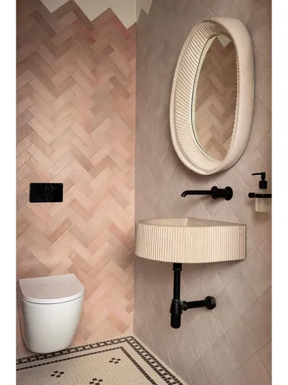Even a compact powder room can make a statement. Here, we combined blush subway tiles in a herringbone pattern with a custom black-and-white mosaic floor. The handcrafted concrete basin and fluted mirror were color-matched to the tiles, creating a unified and visually delightful space.