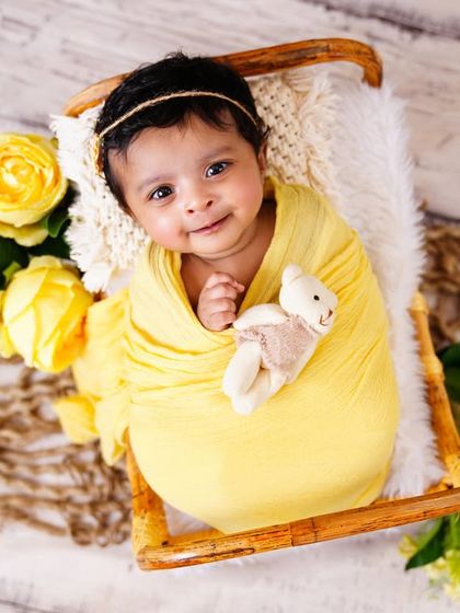 A bright-eyed and smiling newborn wrapped in yellow, holding a small teddy bear. It’s so special when we capture these awake moments.