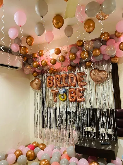 This image shows the full effect of the 'Bride to Be' party decoration in a room. The setup includes a balloon garland on the ceiling, a silver fringe backdrop with foil letters, and balloons scattered on the floor for a complete party look.